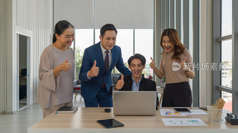 一群成功的商界人士围坐在一张桌子旁，微笑着竖起手指和拇指。领导力的概念。