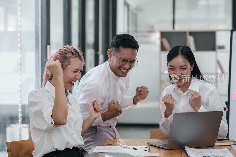 快乐的亚洲商业团队在办公室高举双手庆祝成功。企业胜利和团队成就的理念。
