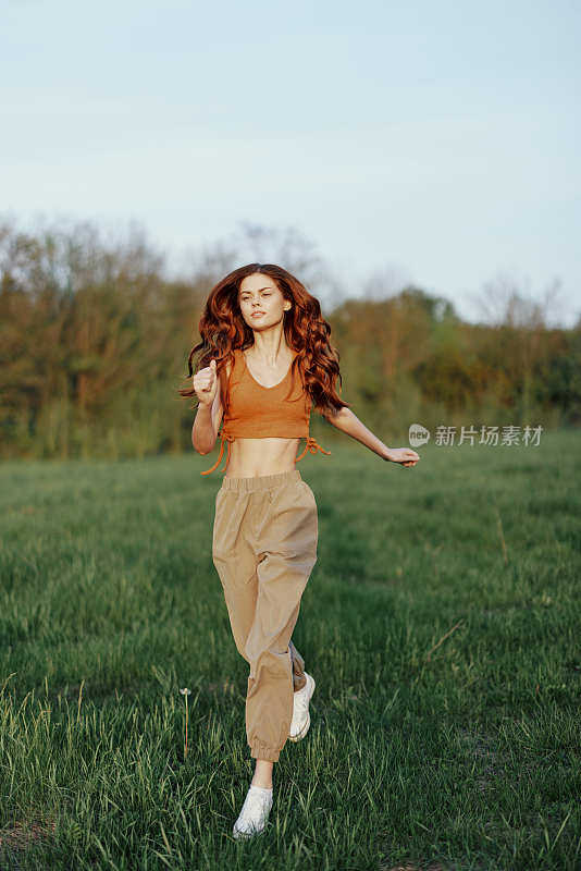 一个身材健美的女人在公园的绿草地上跑着，头发飘散着，在夕阳的余晖中锻炼着