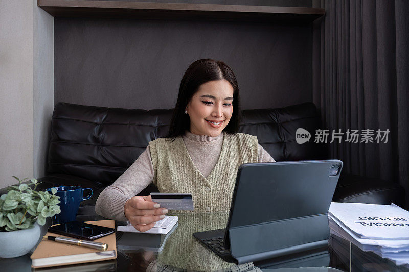 漂亮的年轻女子用笔记本电脑网上购物从家里买东西，用手机通过网上银行应用程序用信用卡支付