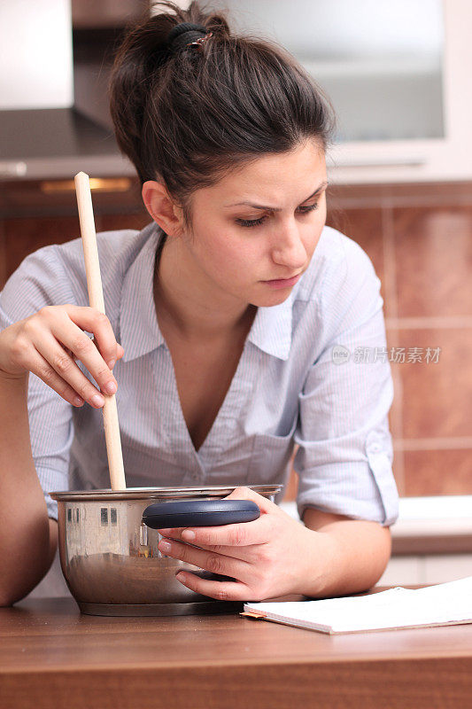 年轻女子一边做饭一边读菜谱