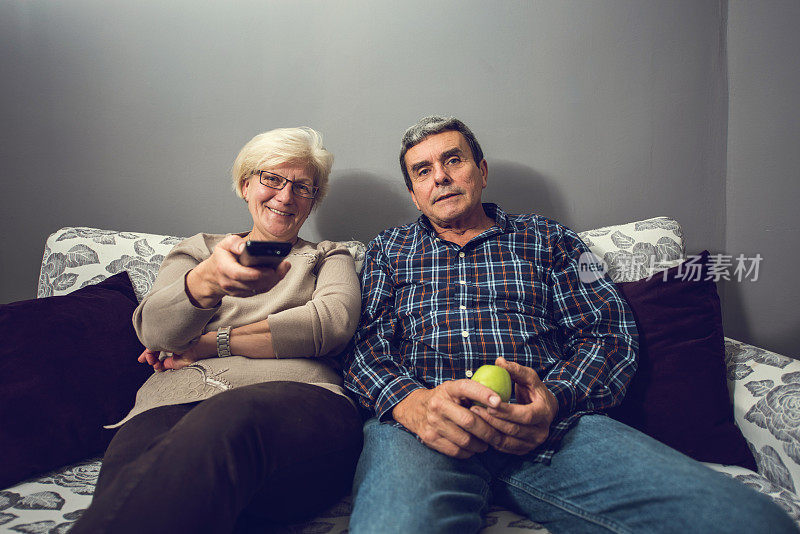 微笑的老夫妇在他们的家里看电视。