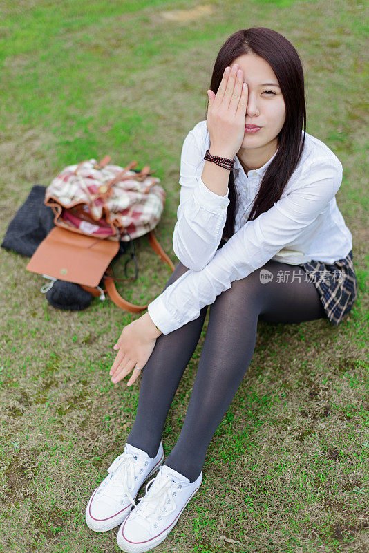 年轻的亚洲女孩拿着书坐在草地上