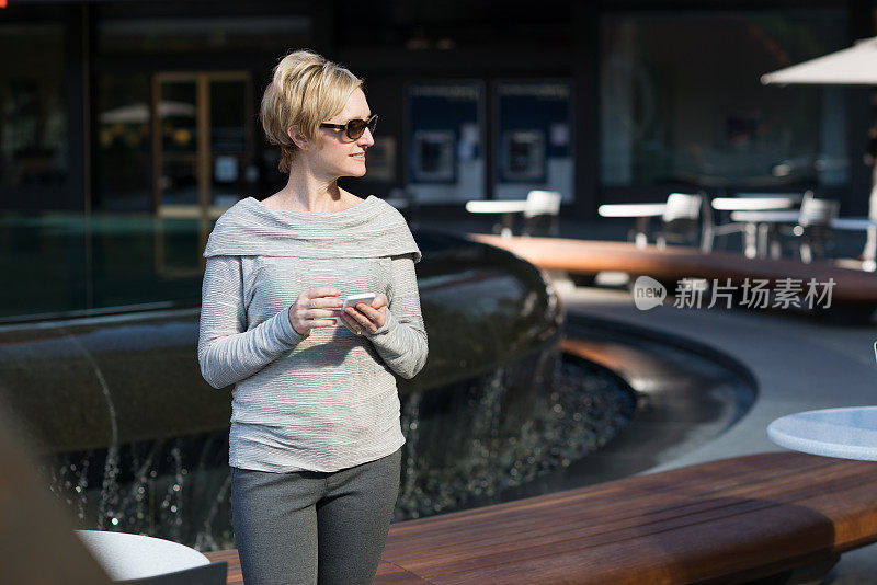 在企业广场，一个成熟的女商人在用她的智能手机