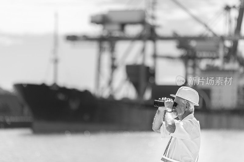 高级商人用双筒望远镜在海港视察工作