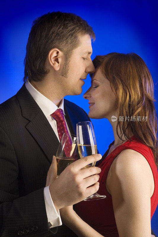 一对穿着考究的浪漫情侣站在蓝色背景下，手里拿着香槟。