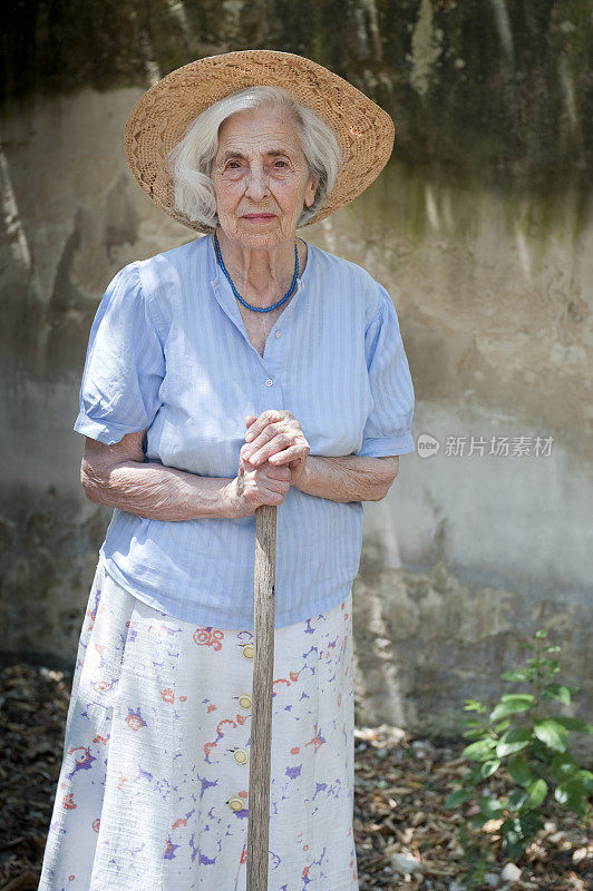 老妇人戴着草帽和木棍在花园里