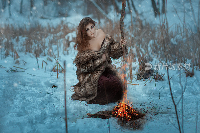 女孩萨满在冬天的森林里被火加热。