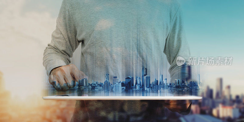 一个在数字平板电脑上工作的人，用全息图描绘未来的现代建筑。日出的城市背景