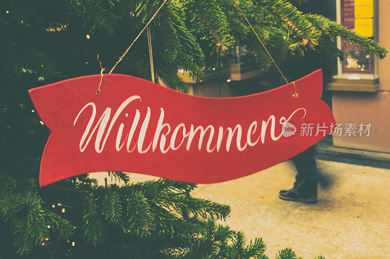 克拉科夫的圣诞树上挂着一块牌子，上面写着欢迎的字样，翻译成德语