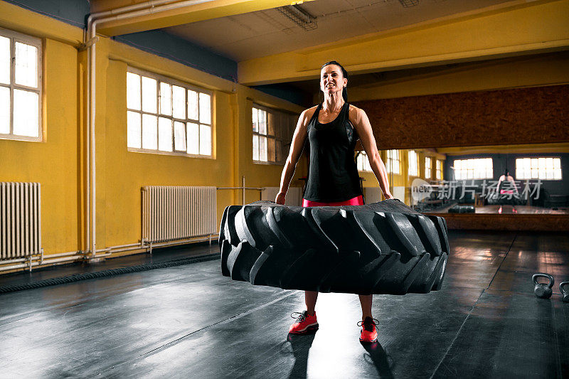 高强度的训练，年轻女子在健身房举着大轮胎