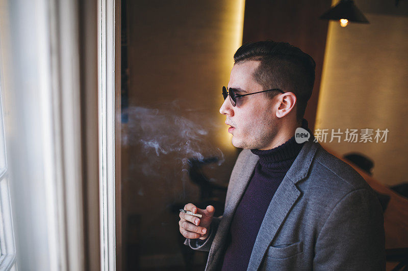 一名黑手党男子在窗边抽烟沉思