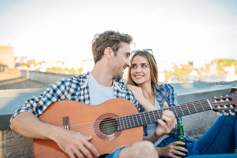 一个年轻人在屋顶上给他的女朋友弹吉他