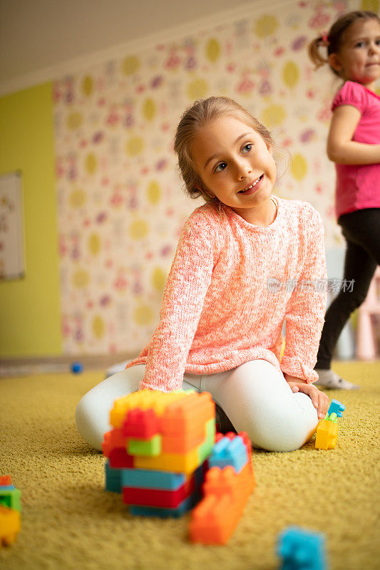 微笑的小女孩在幼儿园玩玩具积木。