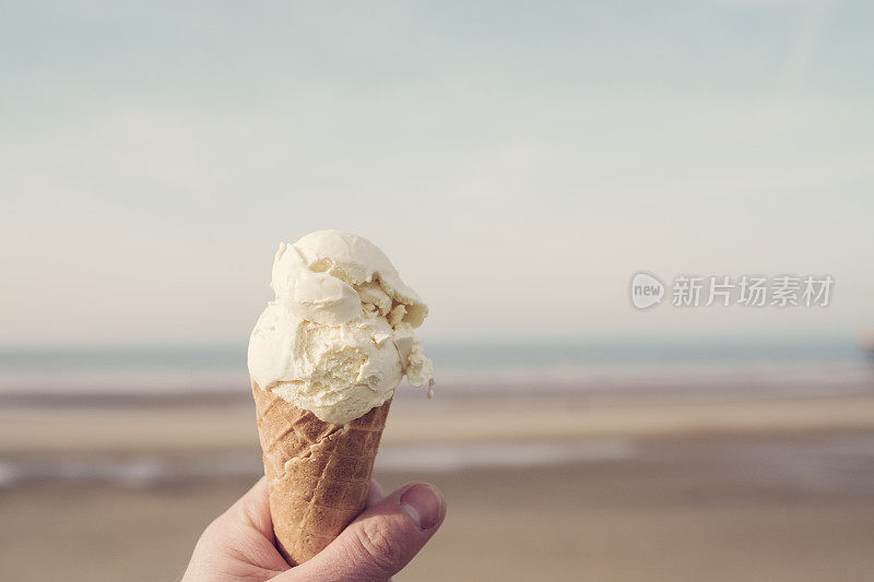 在一个阳光明媚的日子里，退潮时手拿冰淇淋蛋卷俯瞰布莱克浦的海滩。