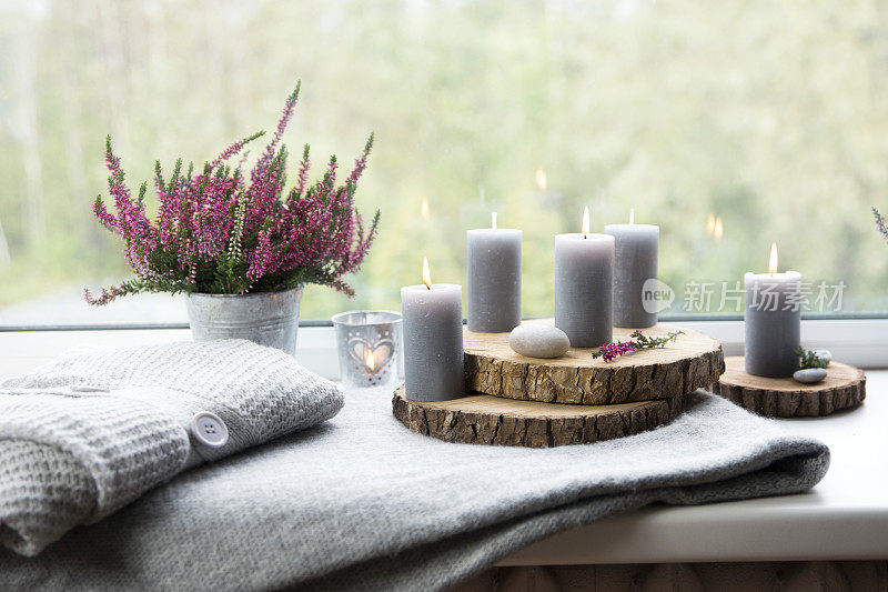 为秋天做准备。舒适的秋天降临在窗台上。灰色的蜡烛，火焰木板，普通的粉色石南花在锌桶花盆。舒适的生活空间概念。