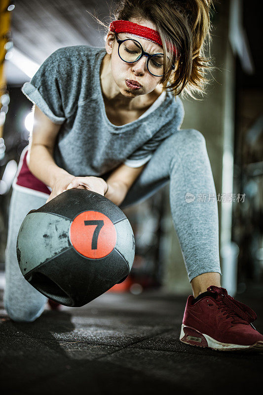 书呆子女运动员试图在体育馆里举起沉重的实心球。