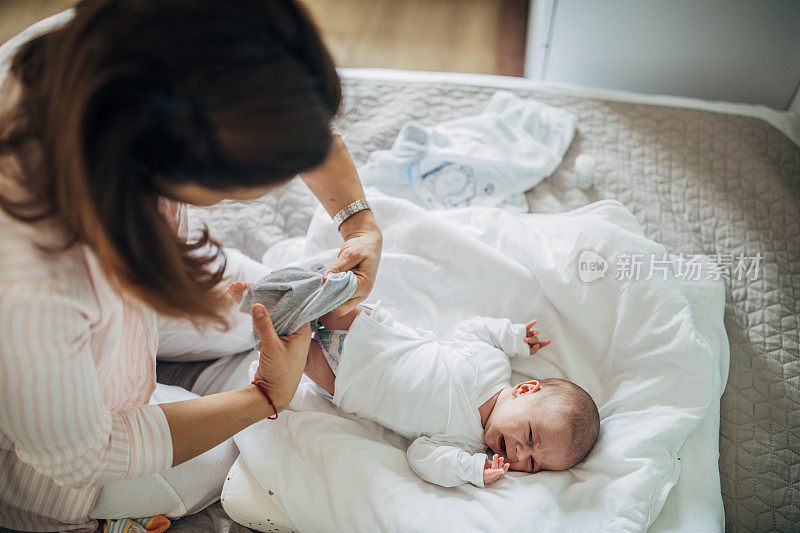 妈妈在卧室的床上给她的男婴换衣服