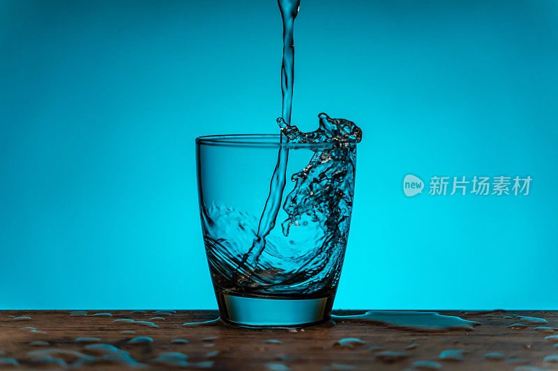 水从水瓶流入玻璃杯-蓝色的背景