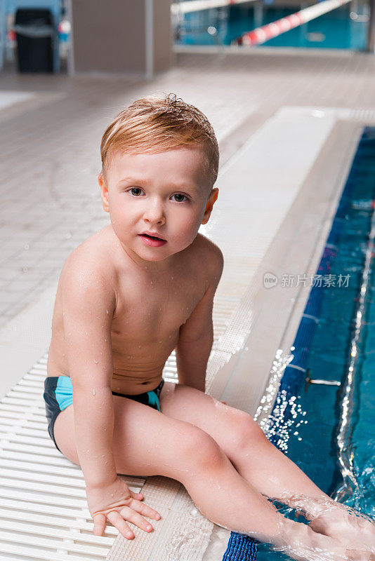 可爱的小男孩坐在游泳池旁边