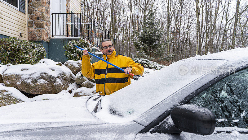 一场雪后，一名男子正在刷雪中的汽车