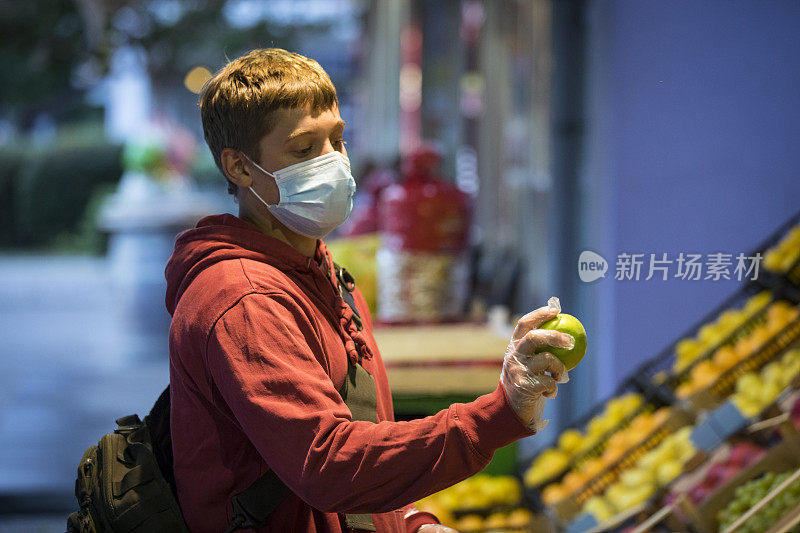 新冠肺炎大流行期间，一名年轻成年男子在城市街道的市场上检查苹果