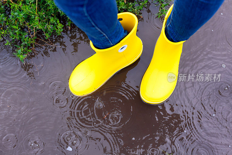 穿着黄色胶靴的女人站在雨中的水坑里。