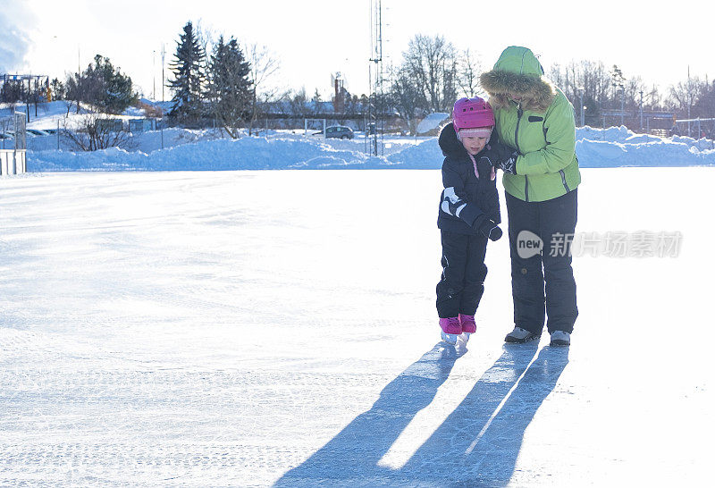 教孩子溜冰。一个年轻的女人在城市的室外溜冰场训练一个小女孩。