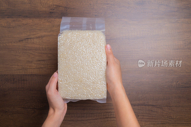 手里拿着装在透明塑料袋里的大米放在木桌上，泰国茉莉花大米。