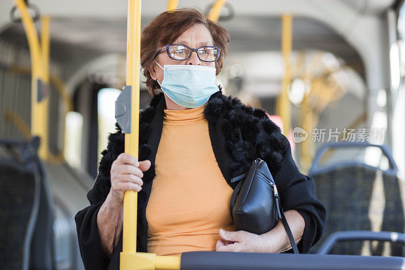 扶着公交车上的一根柱子，戴着防护口罩的老妇人