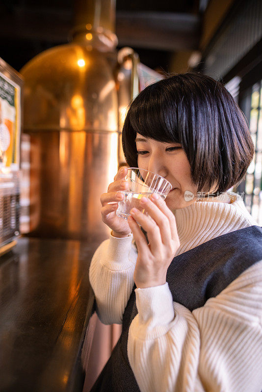 年轻女子喝一杯“saki”(日本米酒)在酒类商店