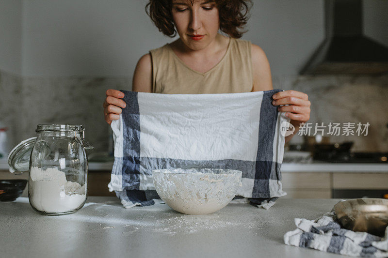 家庭爱好:一个女人从头开始烤酸面包-在面团上放一条厨房毛巾让它休息和证明