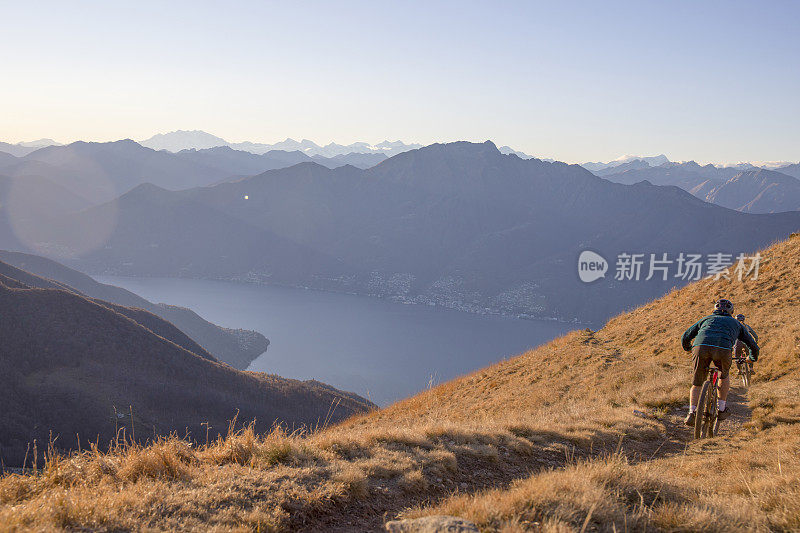 骑山地车的人在日出时从长满草的山脊上骑下来