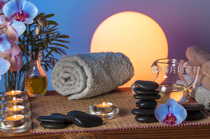 美容spa概念-黑色按摩石，兰花花，蜡烛，毛巾和按摩油在木桌上