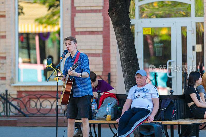 一个年轻人拿着吉他站在中央大街上，弹唱着。2021年5月17日，俄罗斯车里雅宾斯克