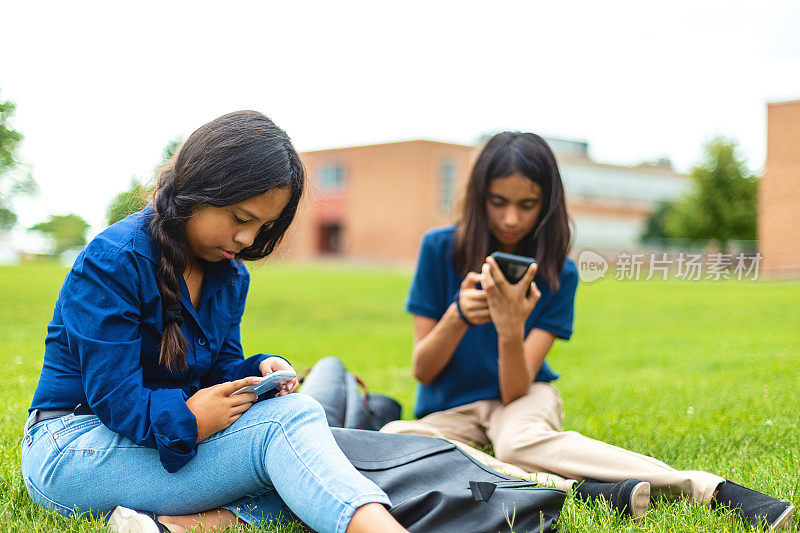 青春期前的女学生坐在校园草坪户外使用技术教育照片系列