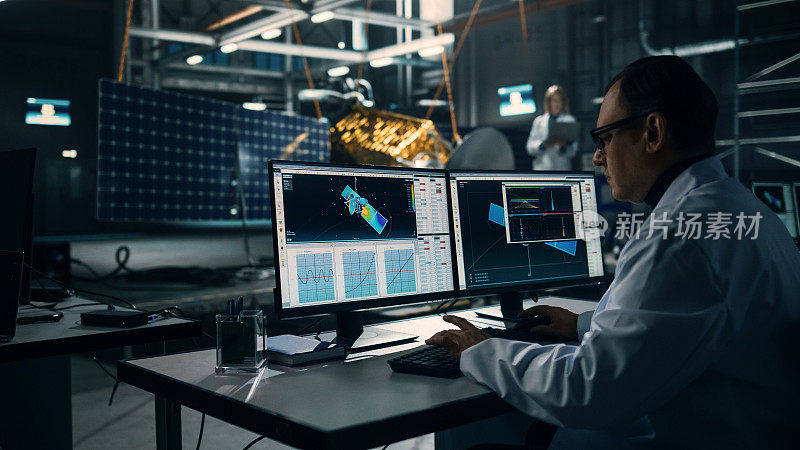 男工程师在建造卫星时使用电脑。航空航天局:科学家正在使用计算机软件编程和组装空间探索任务的航天器。