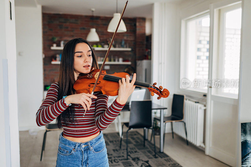 一个专注的女小提琴手享受练习小提琴的正面视图。