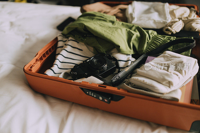 为度假打包必需品:打开装满衣服的手提箱，床上有白色的床单