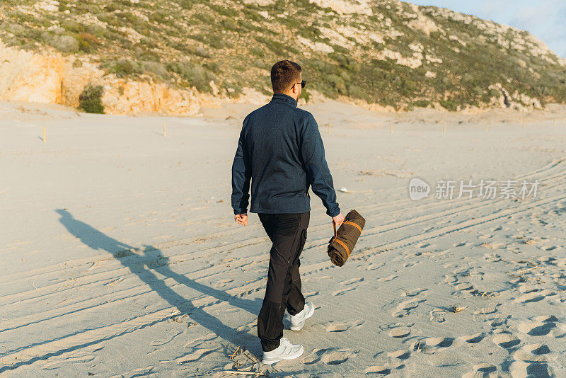 真正的观点，一个人走在海边野餐毯子在日落期间在土耳其