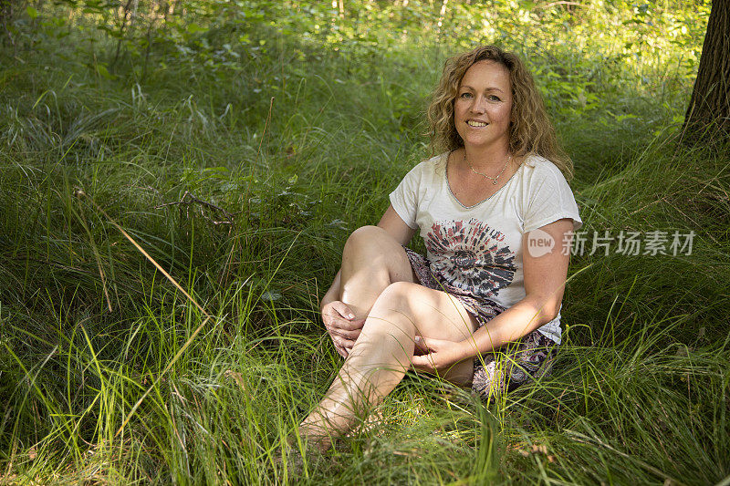 一个四十岁的女人坐在草地上，对着镜头笑