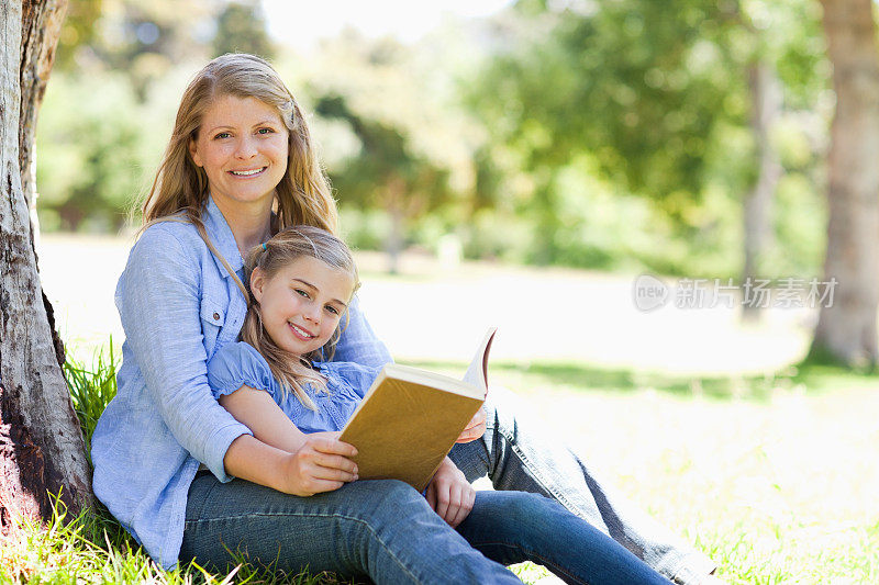 母亲和女儿微笑着读一本书
