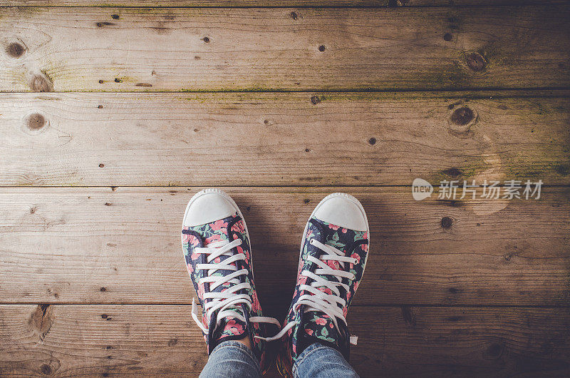 女运动鞋与花卉图案站在木地板上