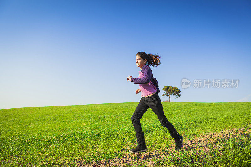 年轻女孩在美丽的绿色田野上奔跑。