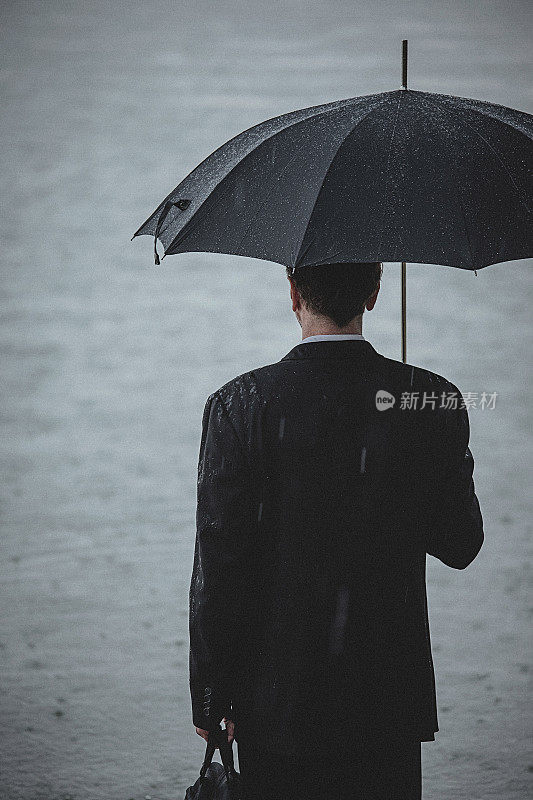 帅气的男人穿着西装，在雨中撑着伞