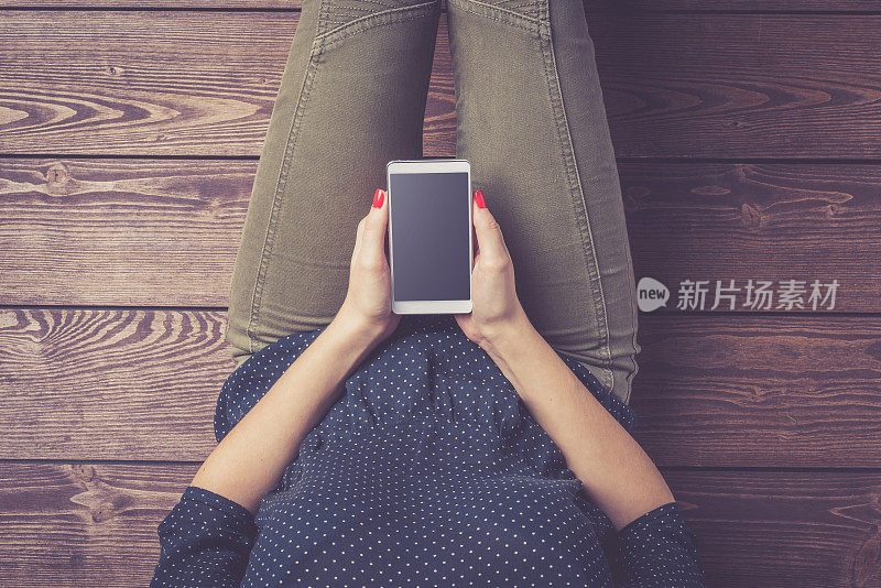 一名年轻女子坐在地板上使用智能手机的照片