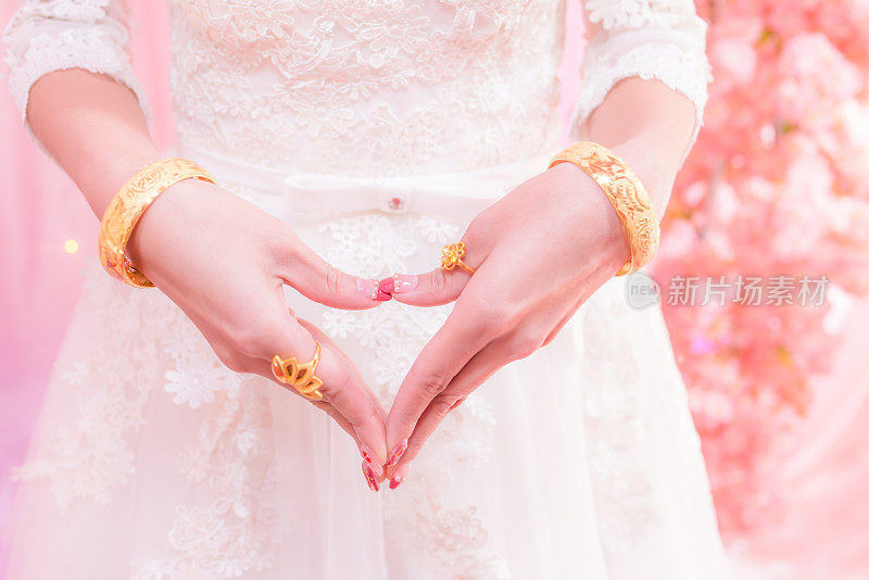 新娘的手呈心形，戴着金结婚戒指和手镯