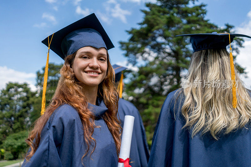 这是一幅年轻女子毕业的照片，她站在其他学生身后，微笑着看着镜头
