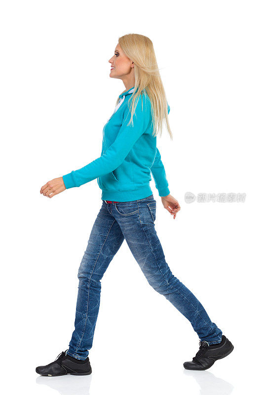 穿着牛仔裤和绿松石衬衫的步行女人。侧视图。