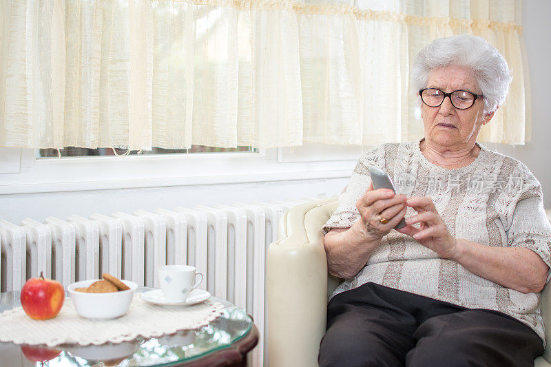 坐在家中扶手椅上用无线电话打电话的年长妇女。